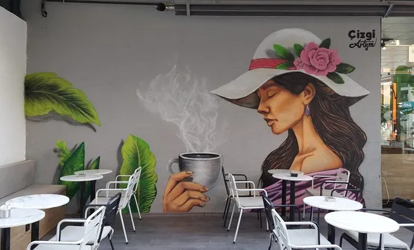 Kafe duvarında şapkalı, elinde buharı tüten kahve tutan kadın portresi